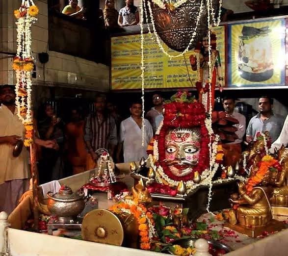 The silver-sheathed Shiva Linga garlanded with marigolds and roses, devotees gathered around it in the sanctum